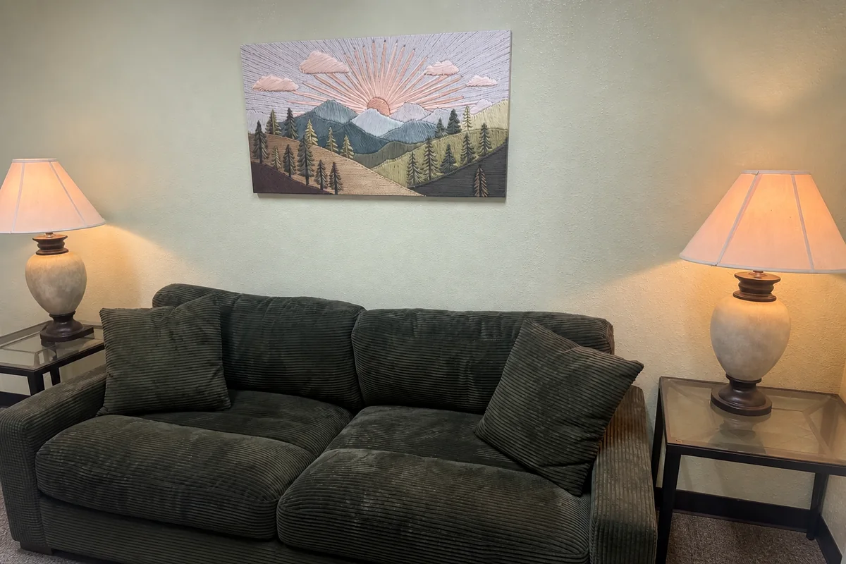 A calm counseling office sitting area with a couch, warm lamp light, and sunrise artwork